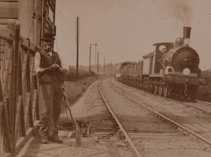 19th century train with telegraph lining the tracks and a worker standing next to a station.